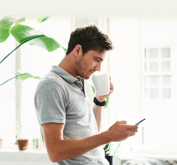 Mann som drikker kaffe mens han holder mobiltelefonen