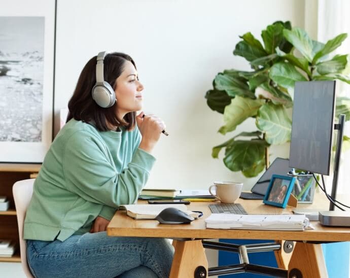 Kvinne med hodetelefoner som holder en penn og ser på en PC-skjerm