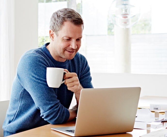 Mann hjemme som bruker bærbar PC og drikker kaffe.