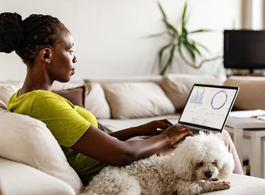 Sittende kvinne med hund, som jobber på en bærbar PC